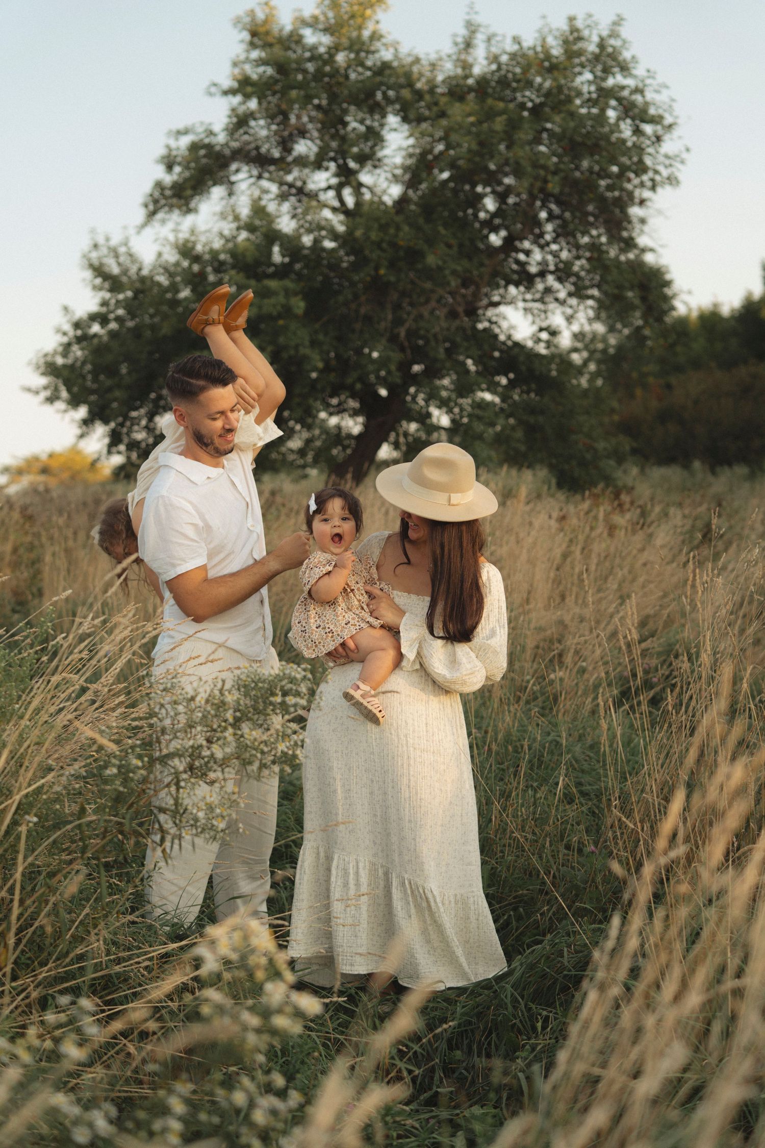 Family enjoying tender moment together in tall grass field at sunset.