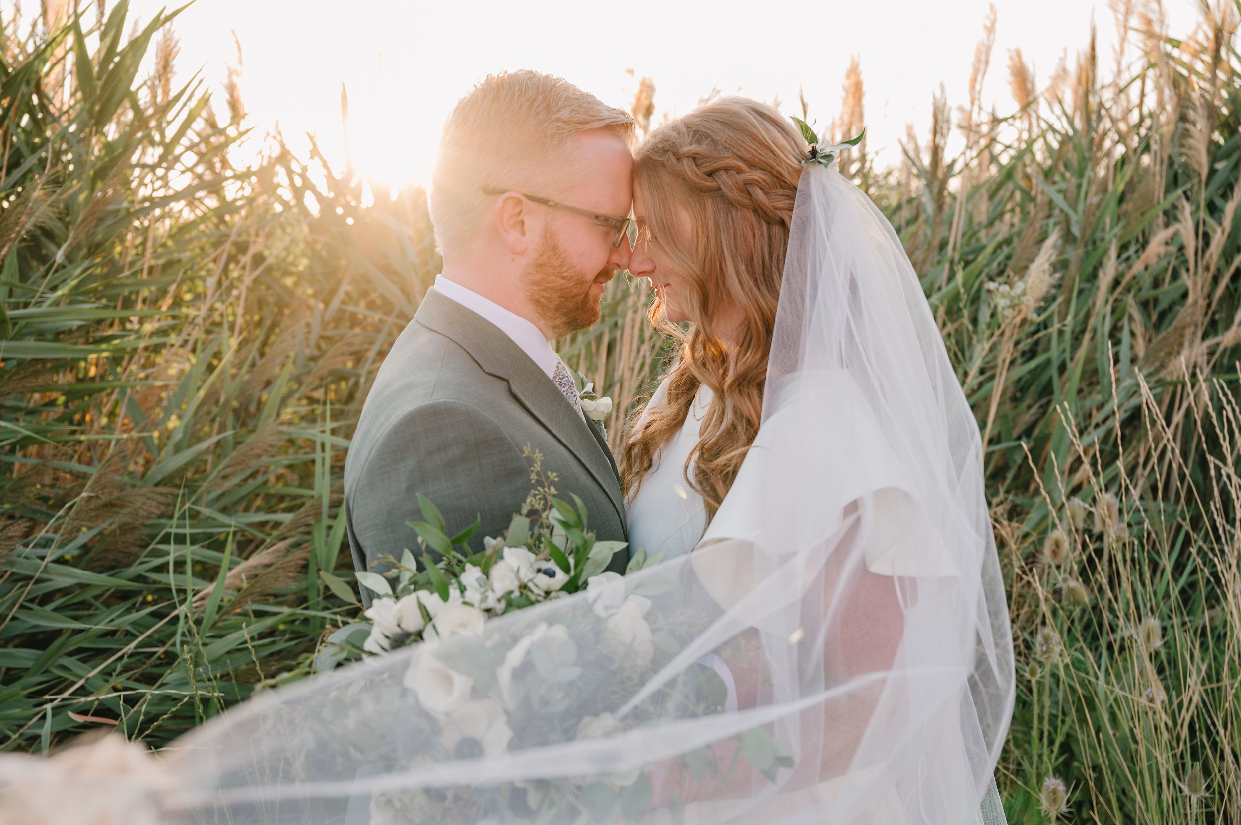 Wedding couple embraces on hilltop with flowing veil and mountain landscape in background.