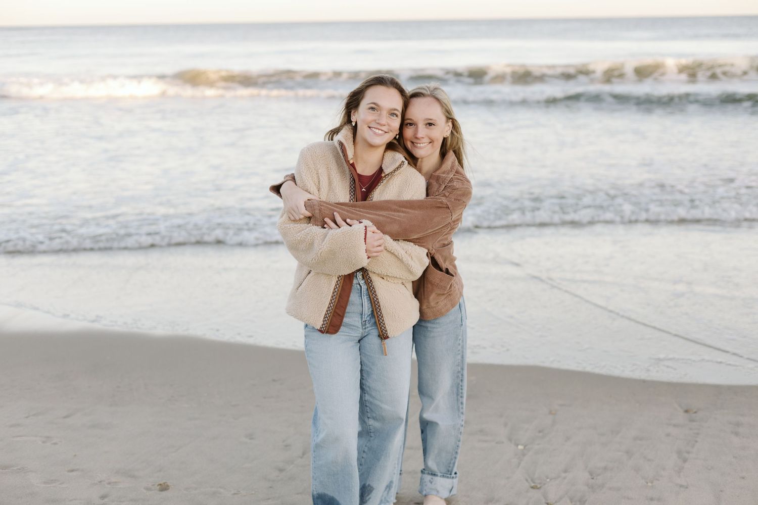 Friends sharing a warm embrace on the beach at sunset.