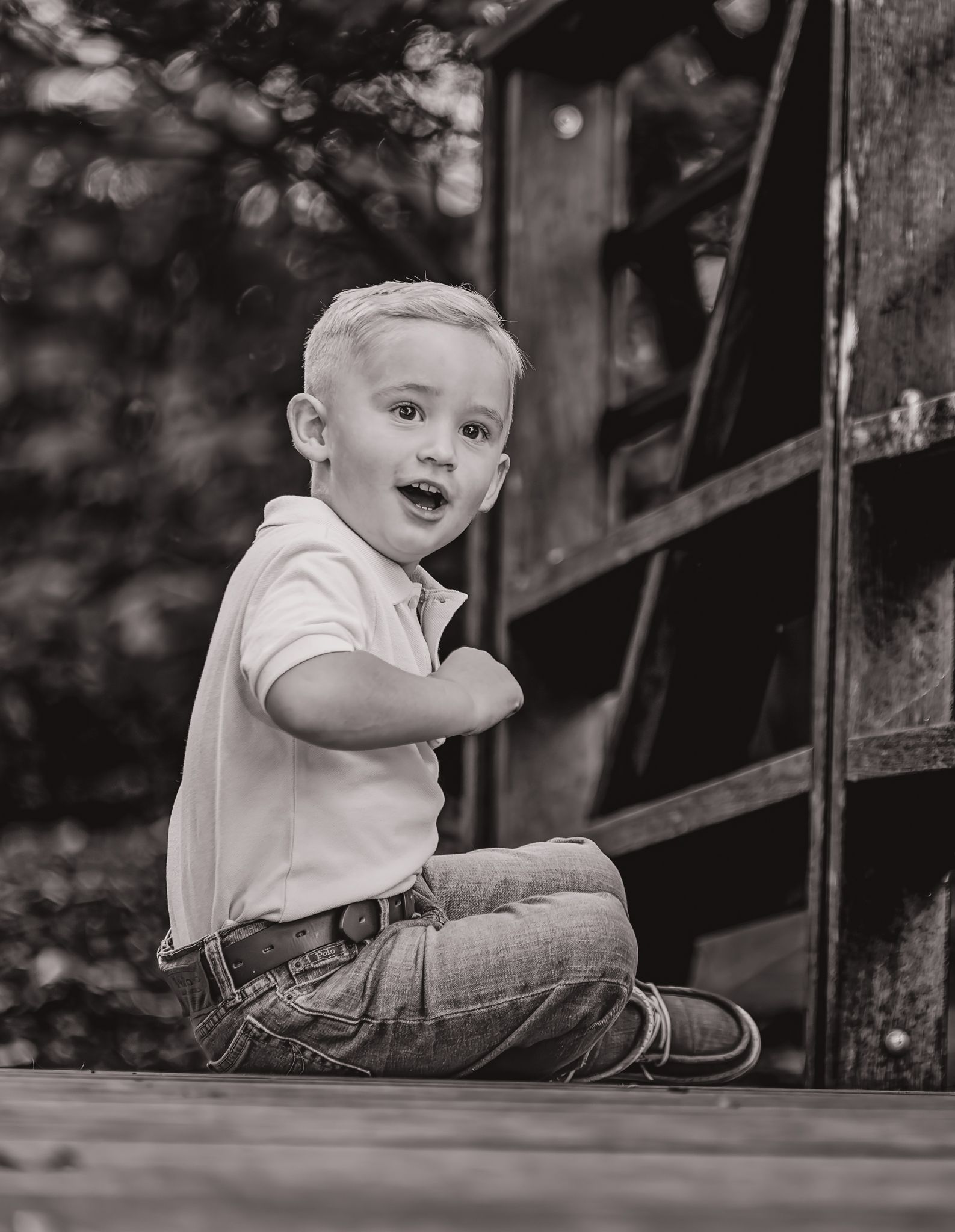 A toddler in a white shirt sits on wooden steps in a black and white photograph.