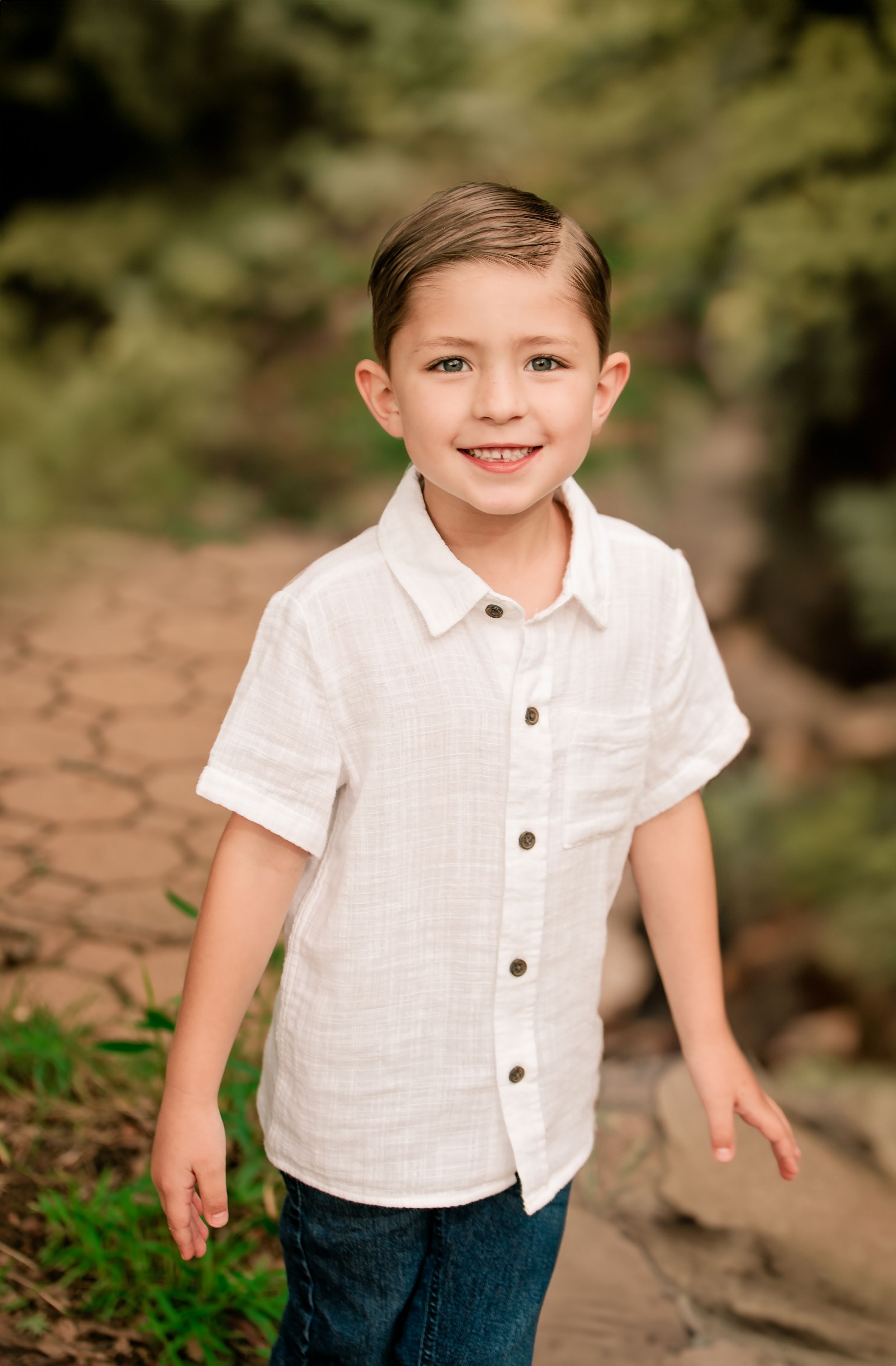A child wearing a white collared shirt sits on natural stone steps surrounded by foliage.