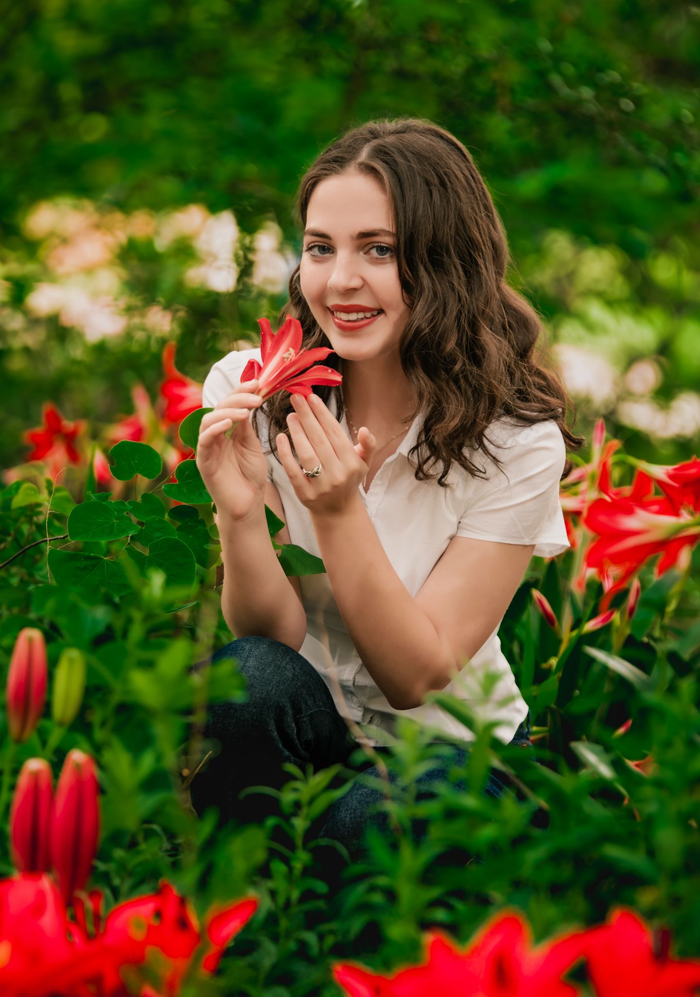 Person in white shirt poses playfully among vibrant red lilies in a lush garden setting.