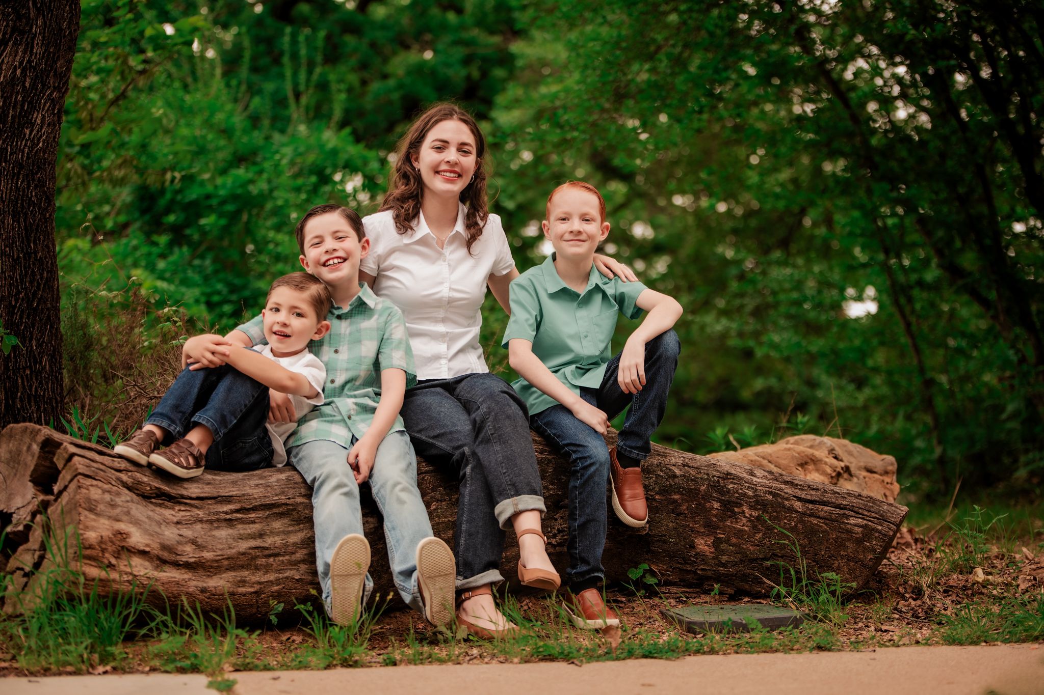 A family sits together on a fallen log in a lush green forest setting during a casual outdoor photo session.
