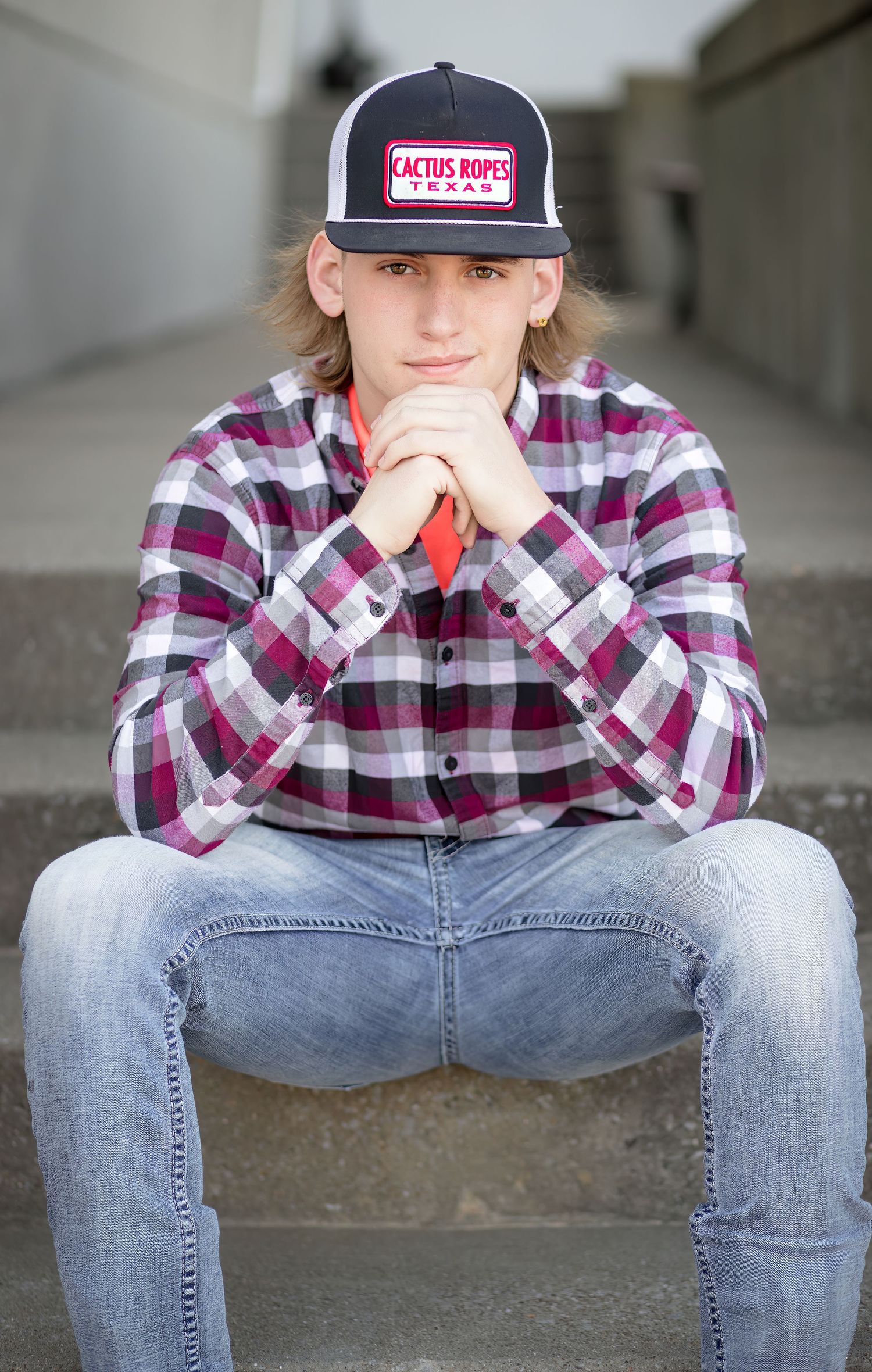 Casual portrait shot of someone in plaid shirt and baseball cap sitting on concrete steps.