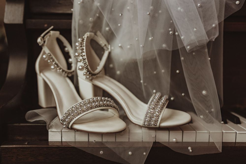Elegant white bridal sandals with crystal embellishments displayed against a dark background.