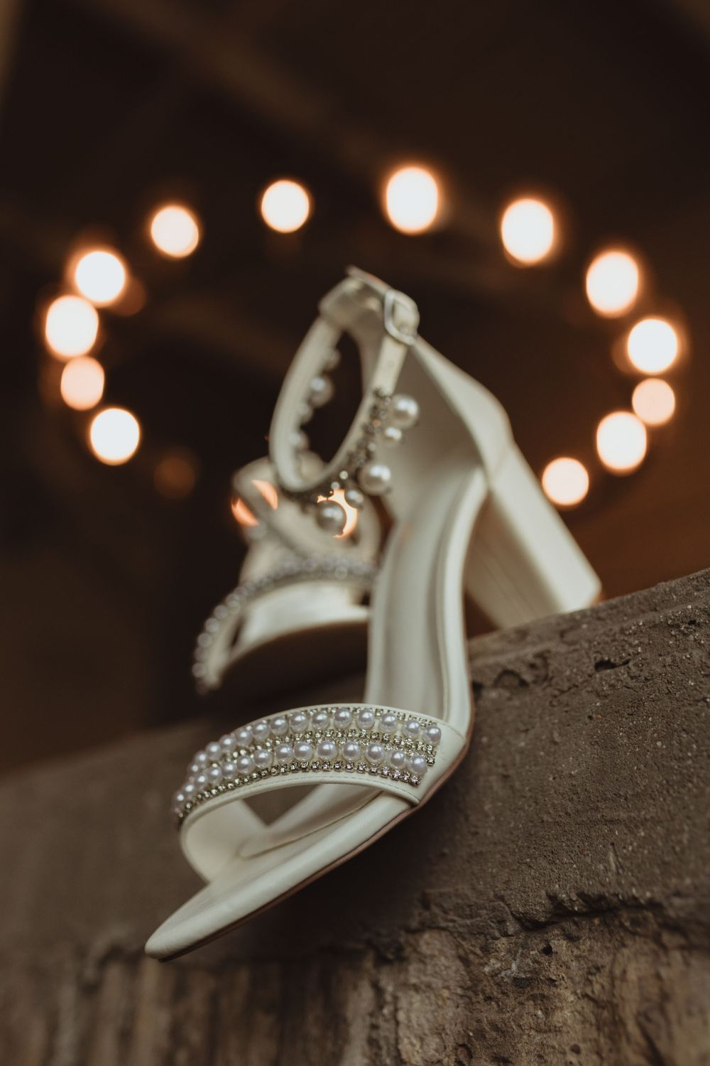 Crystal-embellished wedding shoes photographed with bokeh lights in the background.