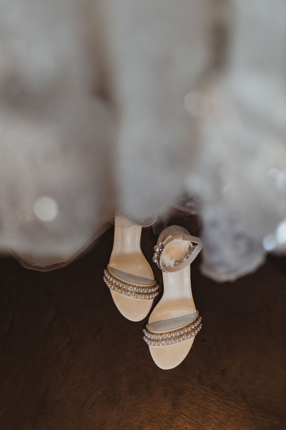 Sparkly bridal shoes peeking out from under a white wedding dress hem.