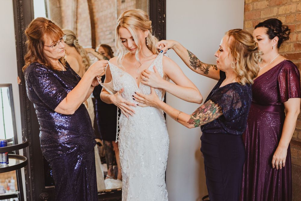 Wedding preparation scene with bridesmaids in purple dresses helping with final touches.