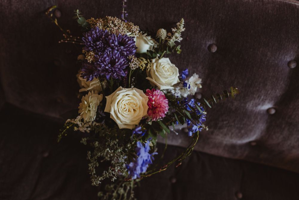 Romantic wedding bouquet with white roses and purple flowers against dark velvet background.