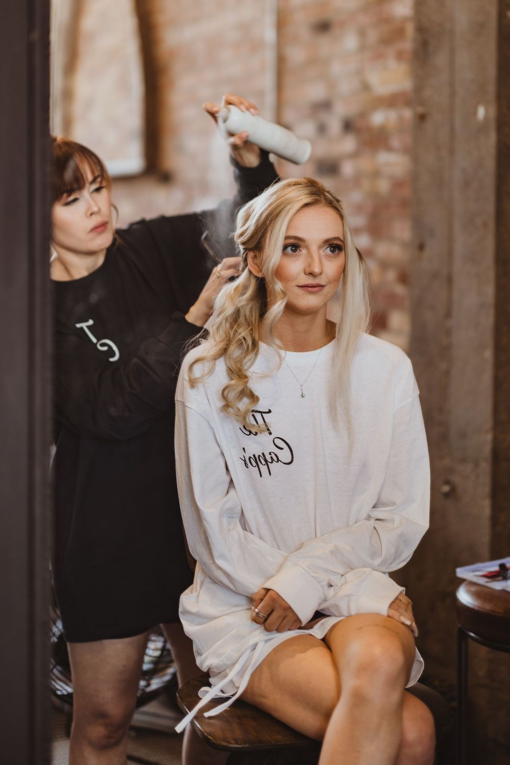 Bride getting ready in white robe before wedding ceremony in brick venue.