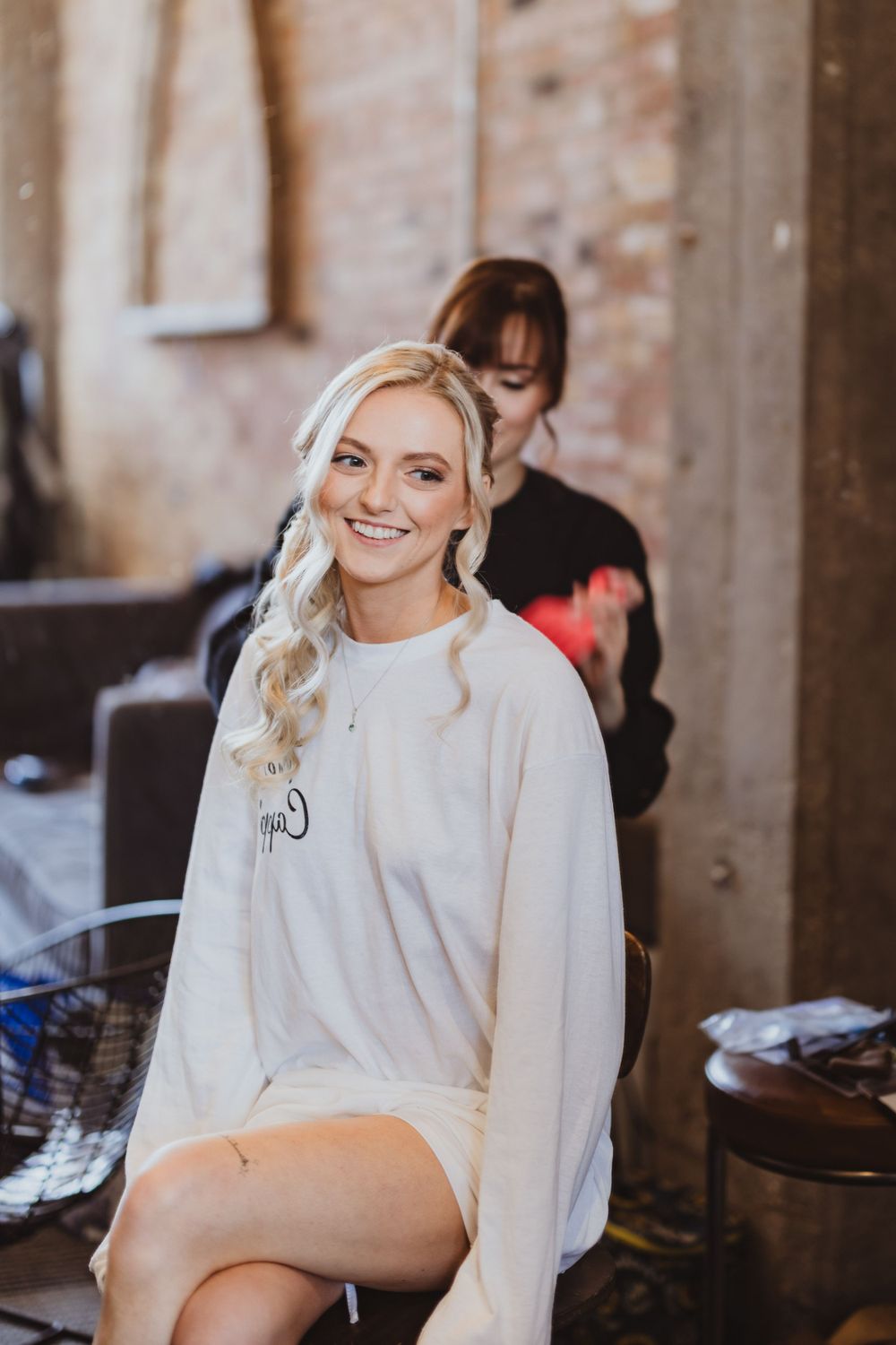 A person in a white robe sits smiling during wedding day preparations.