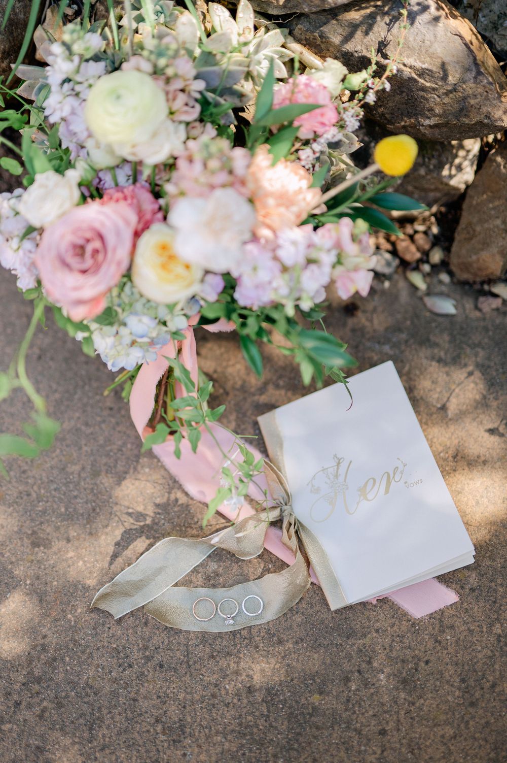 Wedding details featuring a pastel bouquet with roses and a vow book on stone ground.