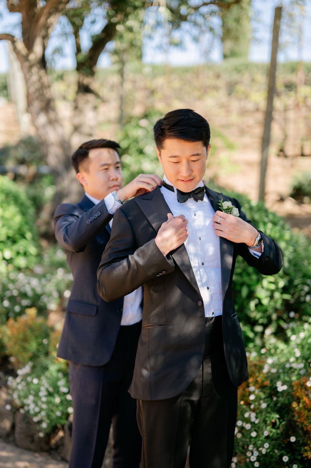 Groomsman helping adjust the groom's bow tie and jacket before the ceremony.