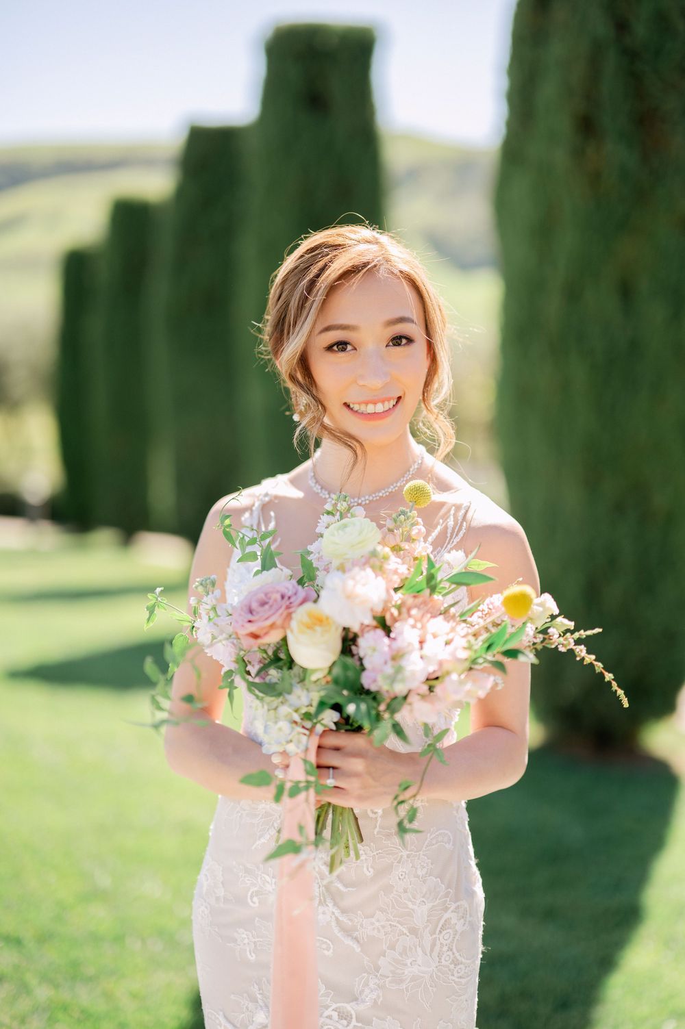 Radiant bride in lace dress holds springtime bouquet with flowing ribbons.