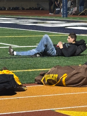 People lying down in formation on a sports field with yellow and white markings.