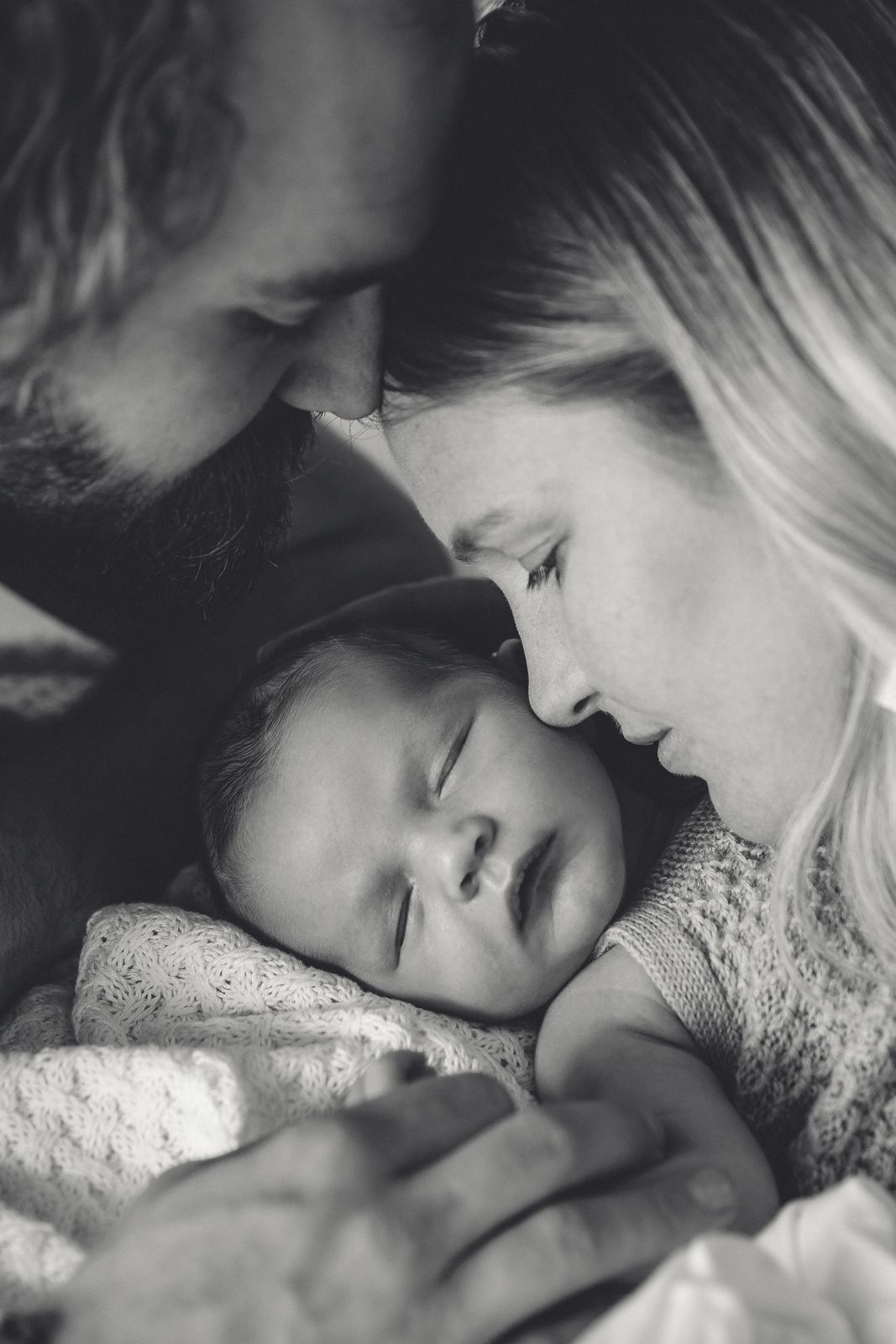 Parents cuddling their newborn baby during a cozy in-home lifestyle photography session in Westport.