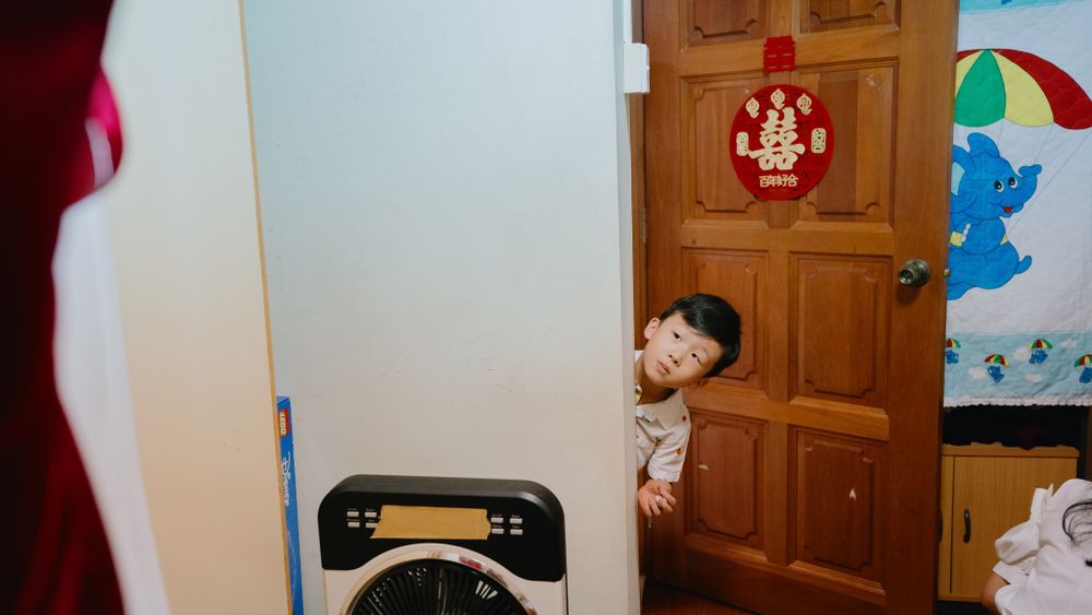 Small child playfully peeking around a wooden door near a washing machine.