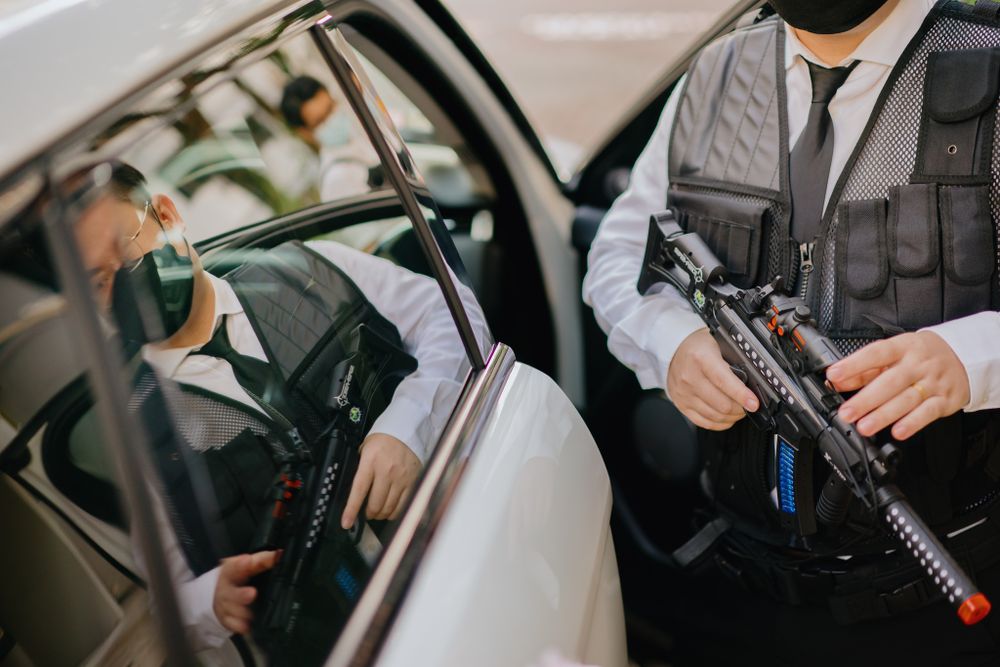 Two people in formal attire holding airsoft guns in a car during a themed photoshoot.