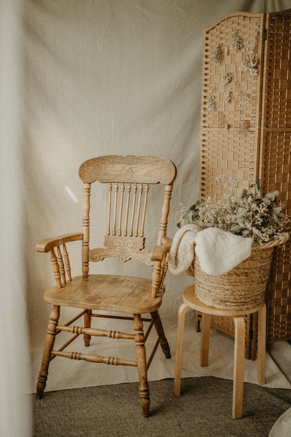 Vintage wooden armchair and small side table with woven basket and dried flowers against neutral backdrop. Maternity studio in Beckenham