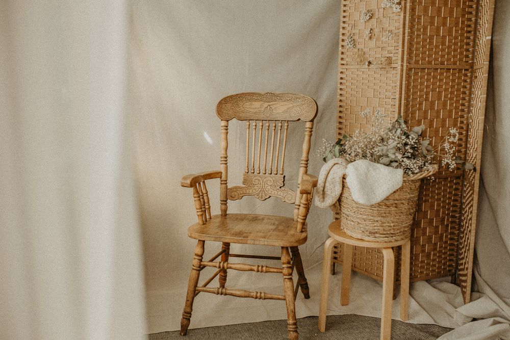 Vintage wooden rocking chair next to small side table with dried flowers against beige fabric backdrop. Maternity studio in Beckenham