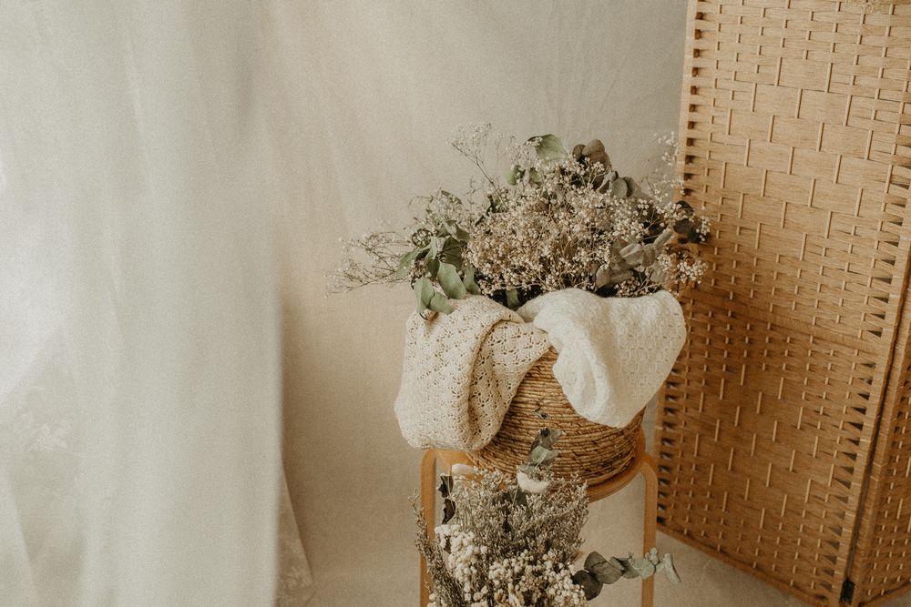 Delicate white baby's breath flowers arranged in a rustic vase with fabric wrapping against a neutral textured backdrop.Maternity studio