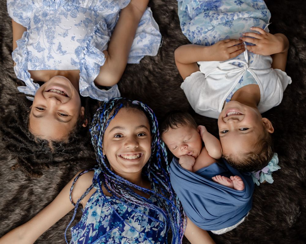 A family lies together on dark fur, wearing coordinating blue outfits in an overhead portrait.