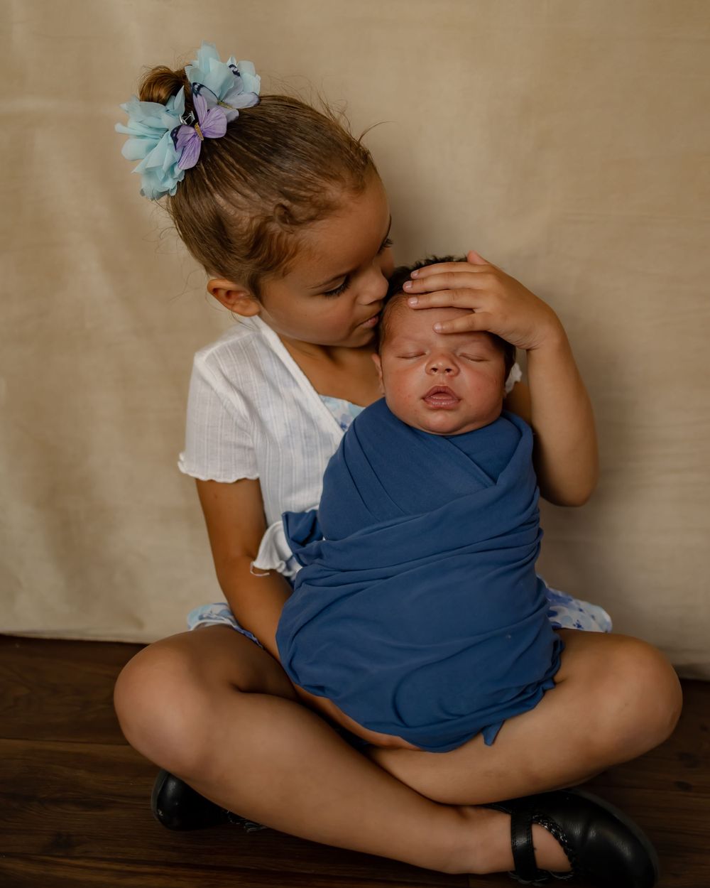 Two children share a tender moment as the older sibling cradles a swaddled baby.