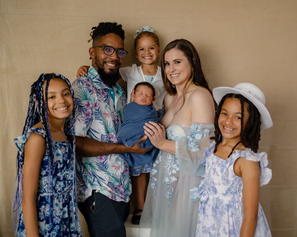 A family poses together in coordinating blue and white outfits against a neutral background.