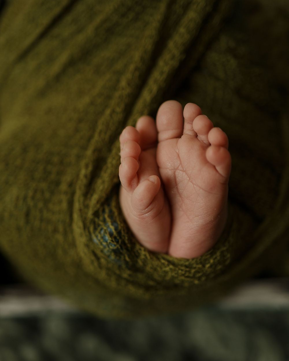 Tiny newborn baby feet peek out from a soft green knitted wrap.