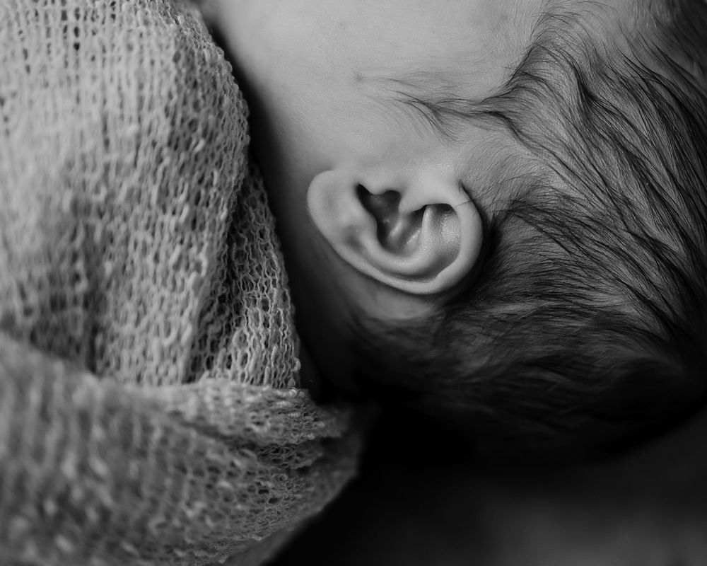 Black and white close-up of a newborn's ear and hair wrapped in knit fabric.