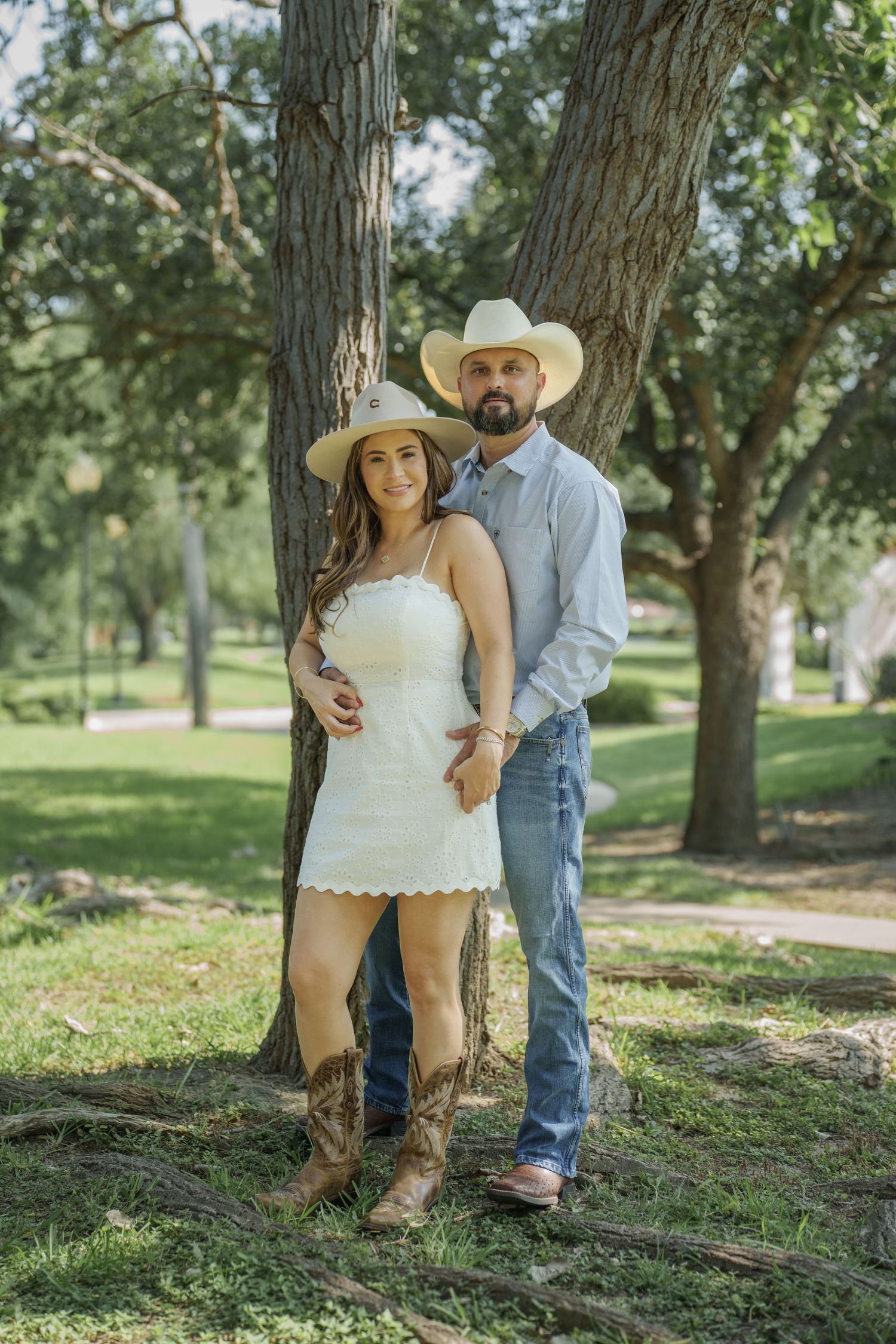 A western-themed engagement photo under trees with cowboy hats and boots.