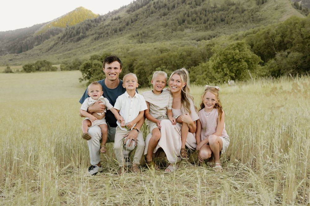A group sits together in a grassy field with mountains in the background on a sunny day.