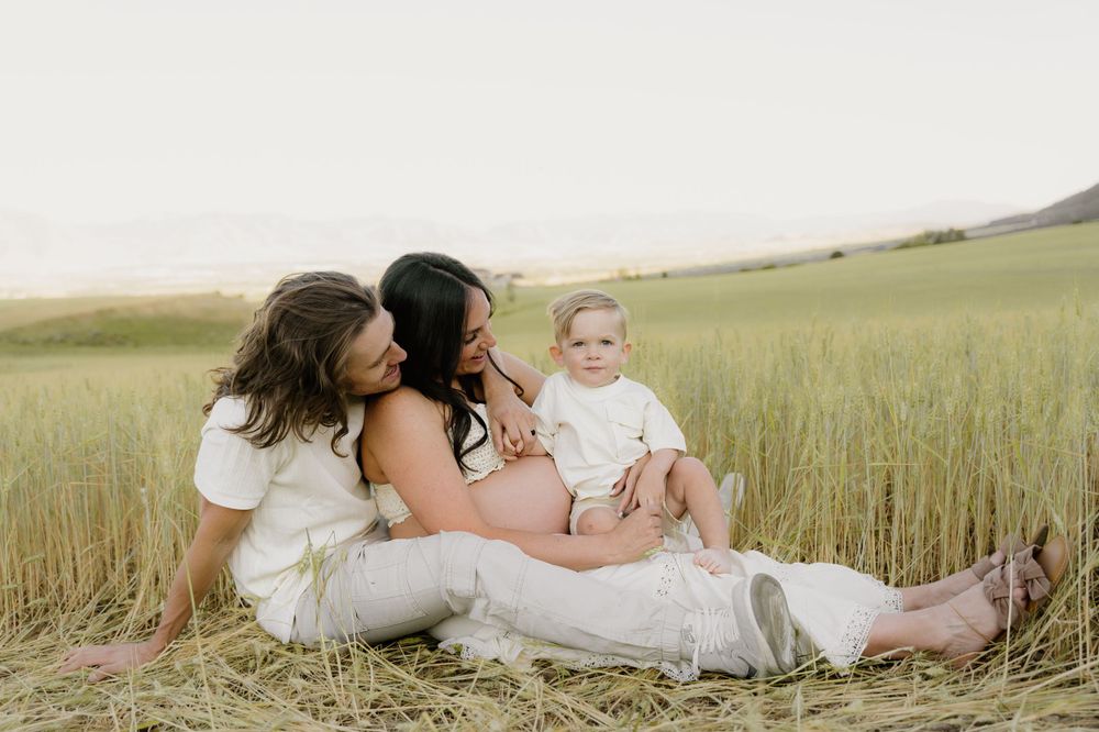 Family sits together in tall golden grass field sharing intimate moment.