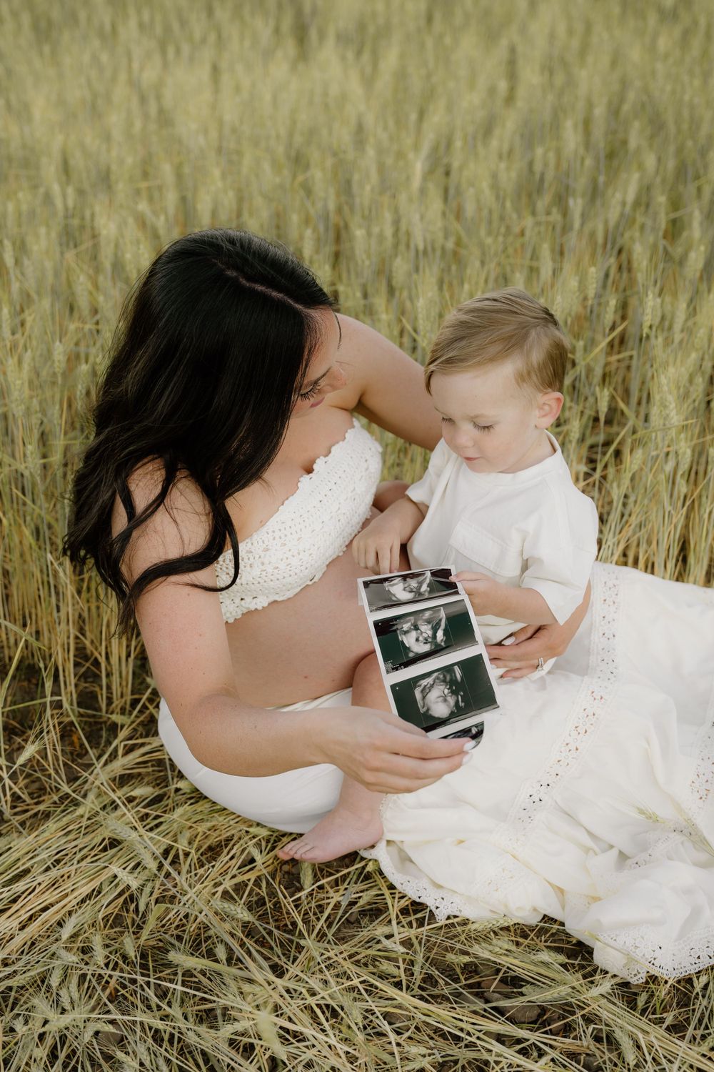 Touching moment as mother and child look at ultrasound photos in wheat field.