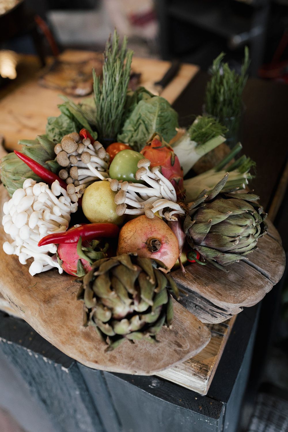 Fresh artichokes, mushrooms and vegetables arranged on rustic wooden boards in an artistic display.