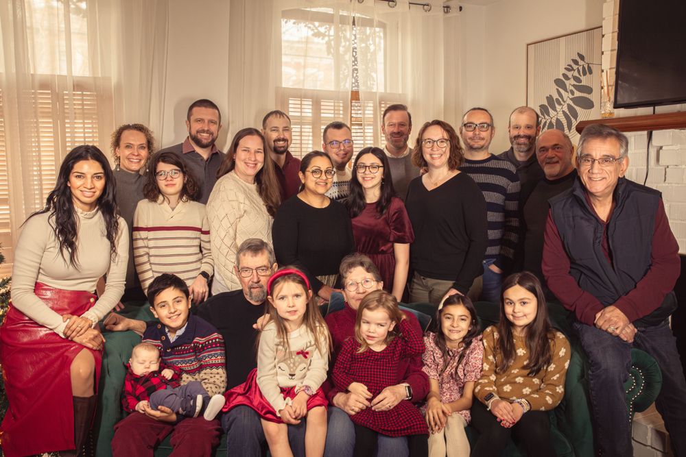 Extended family gathering in living room wearing coordinated burgundy and neutral holiday attire.