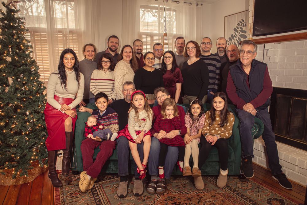 A large family gathering poses together by a Christmas tree in a cozy living room.