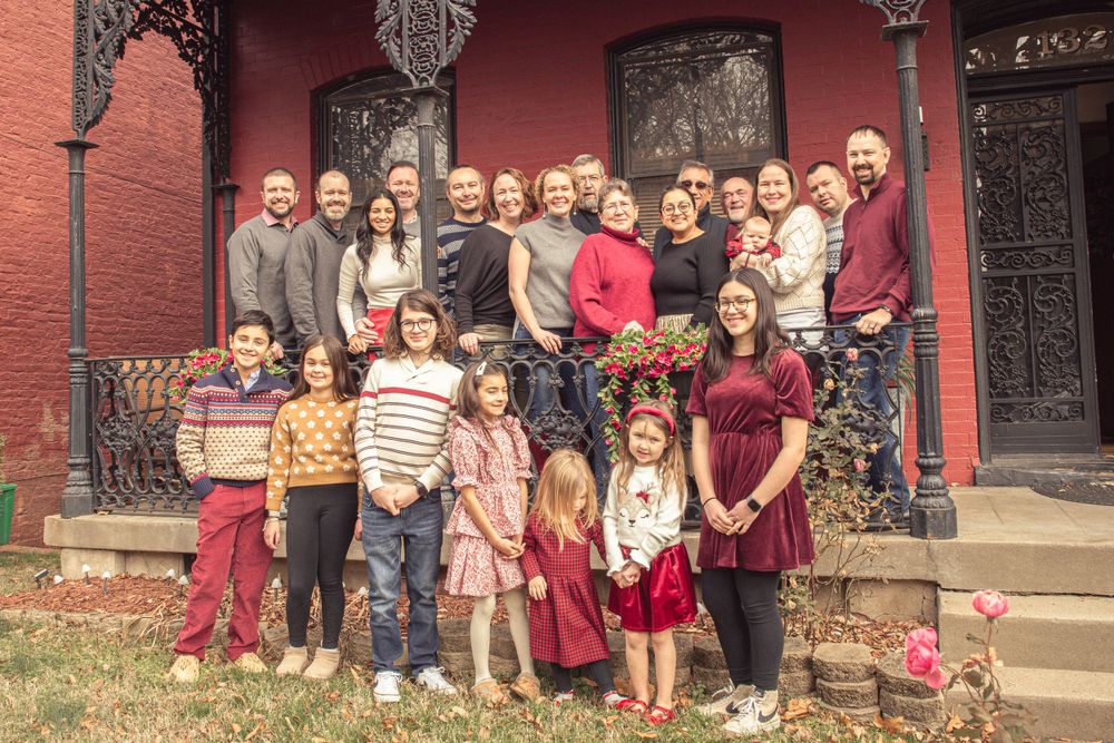 Large family group poses together on vintage brick steps wearing coordinated red and neutral colored outfits.