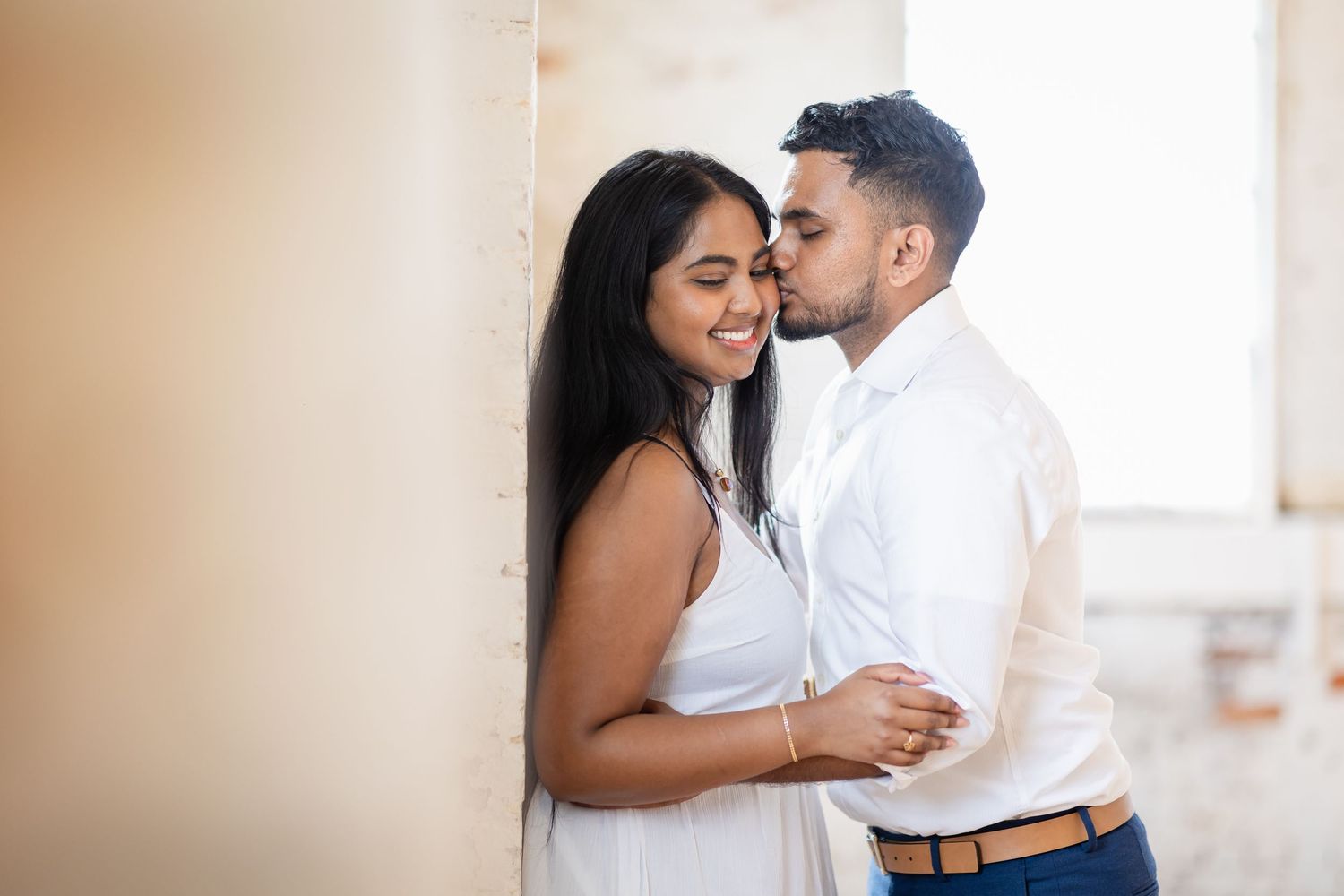 A romantic couple shares an intimate moment against a light colored wall.