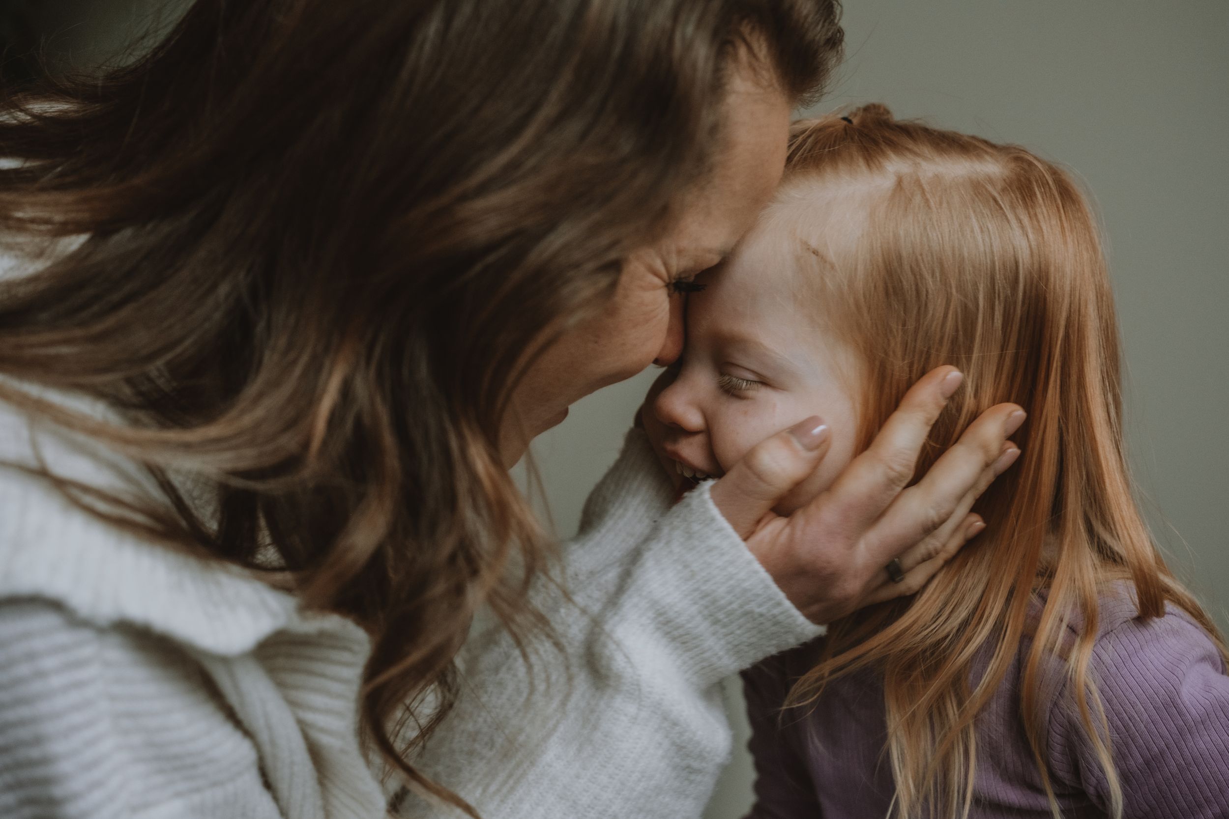 Mother and red-haired daughter sharing tender forehead-to-forehead moment, close-up portrait.