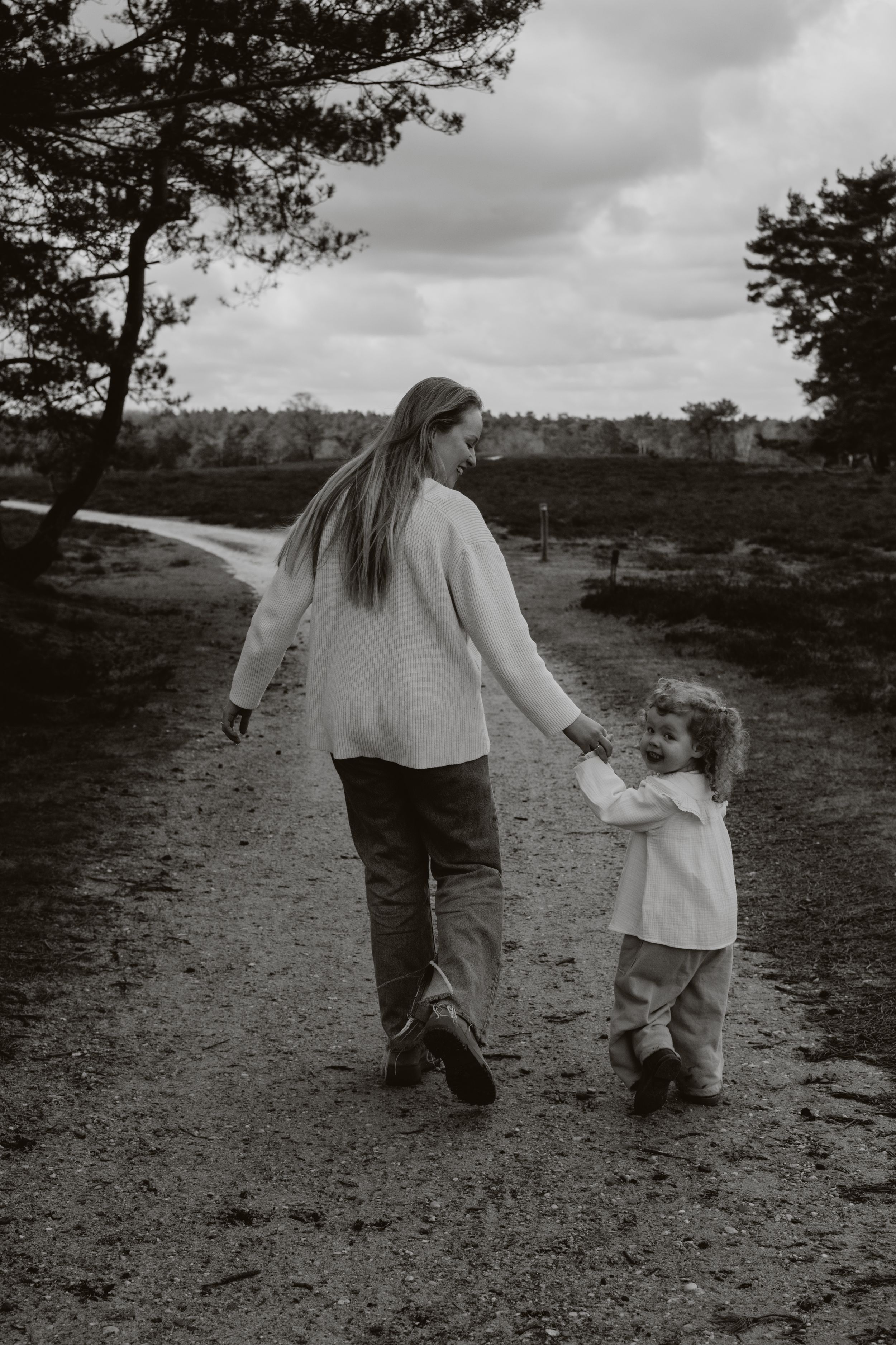 Black and white photo of a mother and young child holding hands walking on a nature path.