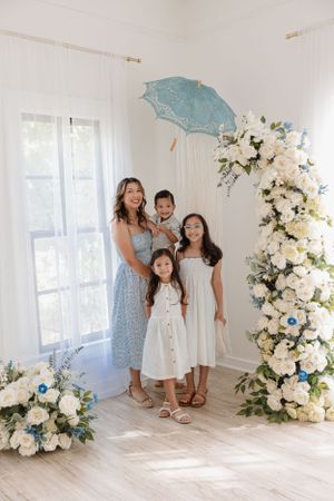 Light-filled indoor portrait setup with blue parasols and cascading white floral arrangements.