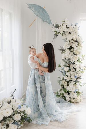 Elegant portrait in a light-filled room with blue parasol and cascading white floral arrangements.