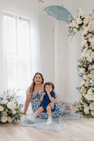 A sweet family moment captured in a white room with blue parasol and floral decorations.