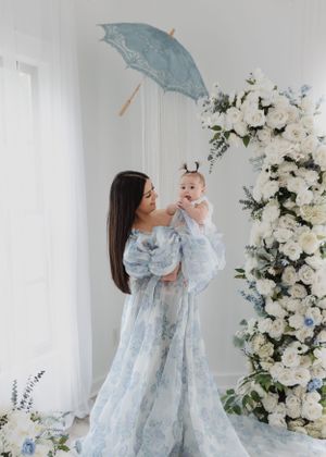 Ethereal photo with flowing blue dress against white floral backdrop and vintage parasol.