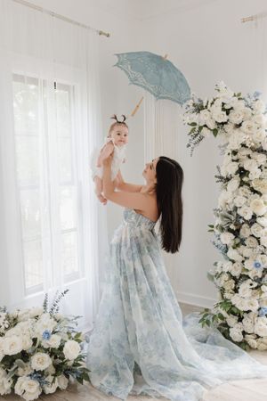 Joyful moment captured in a light-filled studio with blue parasol and white floral arrangements.