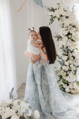 Tender moment in a light-filled studio with cascading white flowers and blue parasol decor.