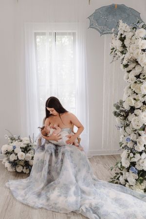 Intimate portrait with flowing blue dress against white floral backdrop and vintage parasol.