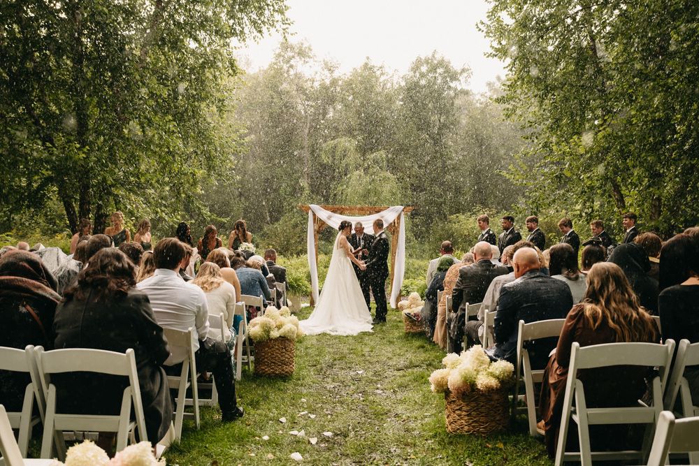 A panoramic view of an outdoor wedding ceremony in a lush green garden setting with white chairs and floral decorations.