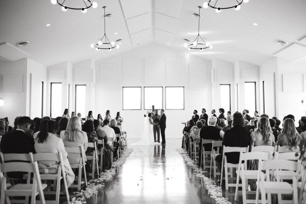 Indoor wedding ceremony in a bright white chapel with guests seated in rows beneath crystal chandeliers.